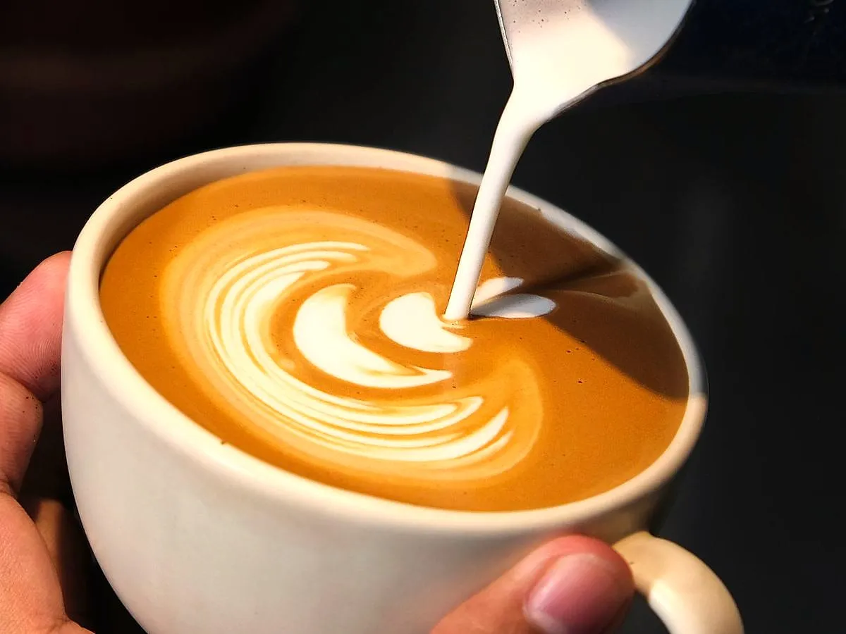Baristas pila pieną į puodelį ir piešia raštą kavos paviršiuje