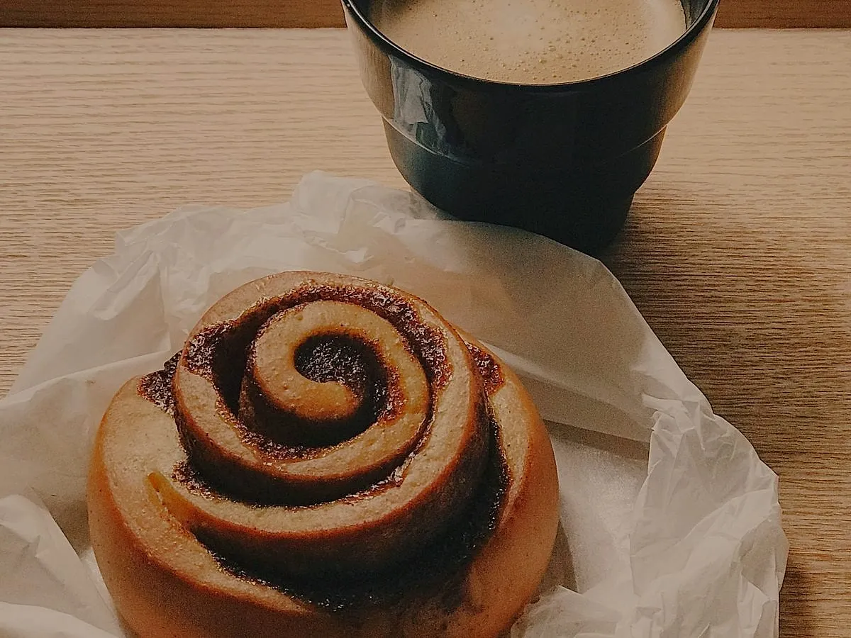 Cinamoninė bandelė ant popieriaus ir juodas puodelis kavos